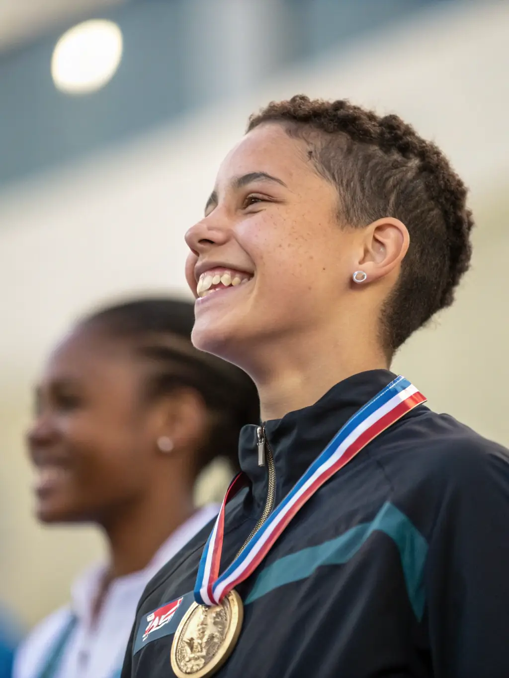 A close-up of a student receiving a medal from a coach, with proud teammates applauding in the background, illustrating personal achievement and growth.