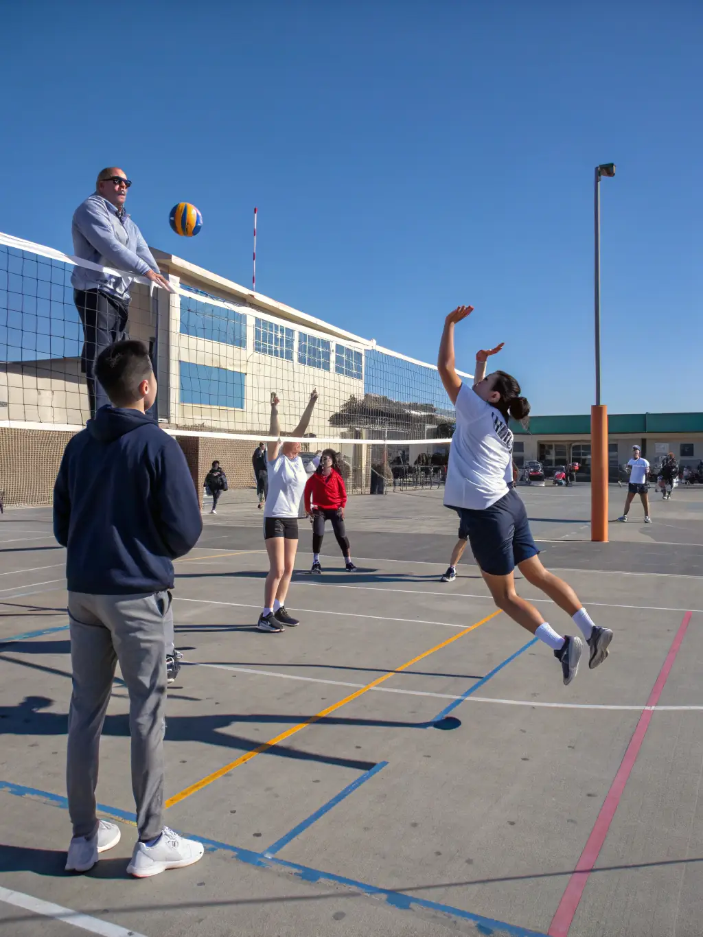 An inclusive scene of students of different backgrounds playing volleyball together, with a coach guiding and encouraging everyone, highlighting a welcoming atmosphere.